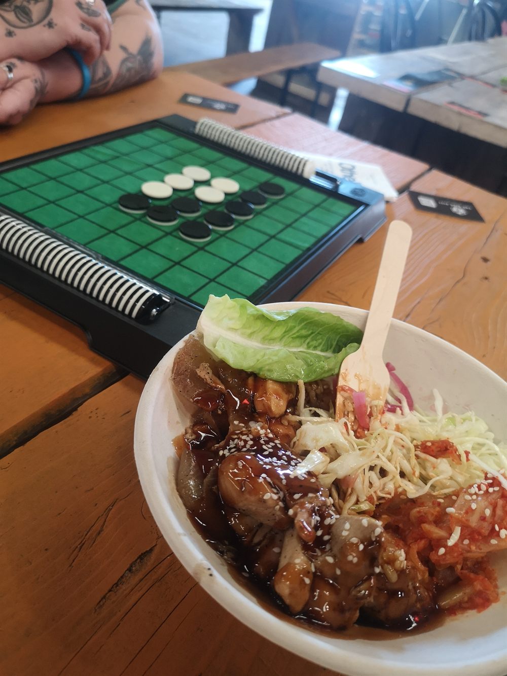 Food from The Pitt Market beside a board game on a wooden table.
